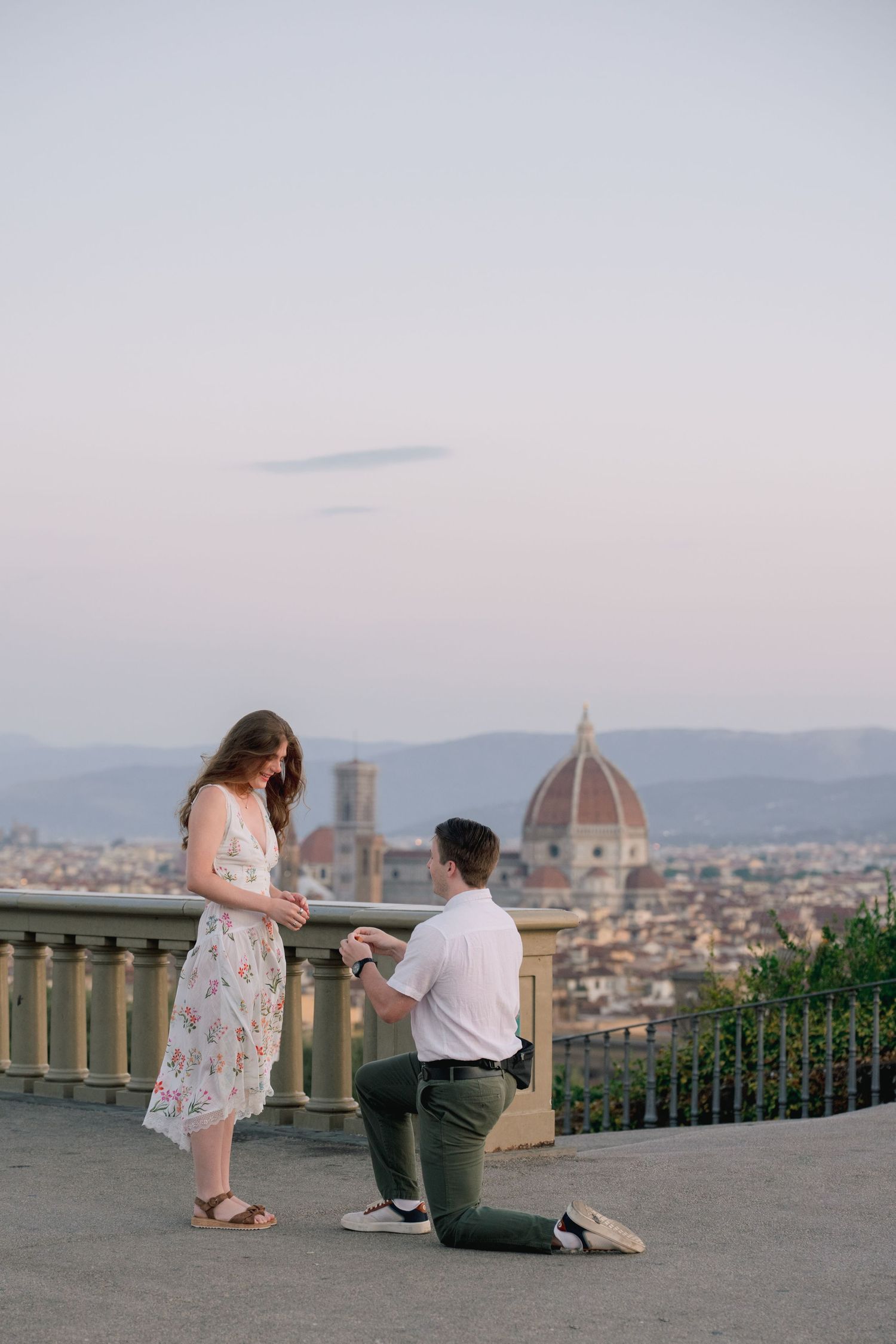 Man proposing on one knee to woman on a terrace with Florence cathedral dome skyline at sunset.