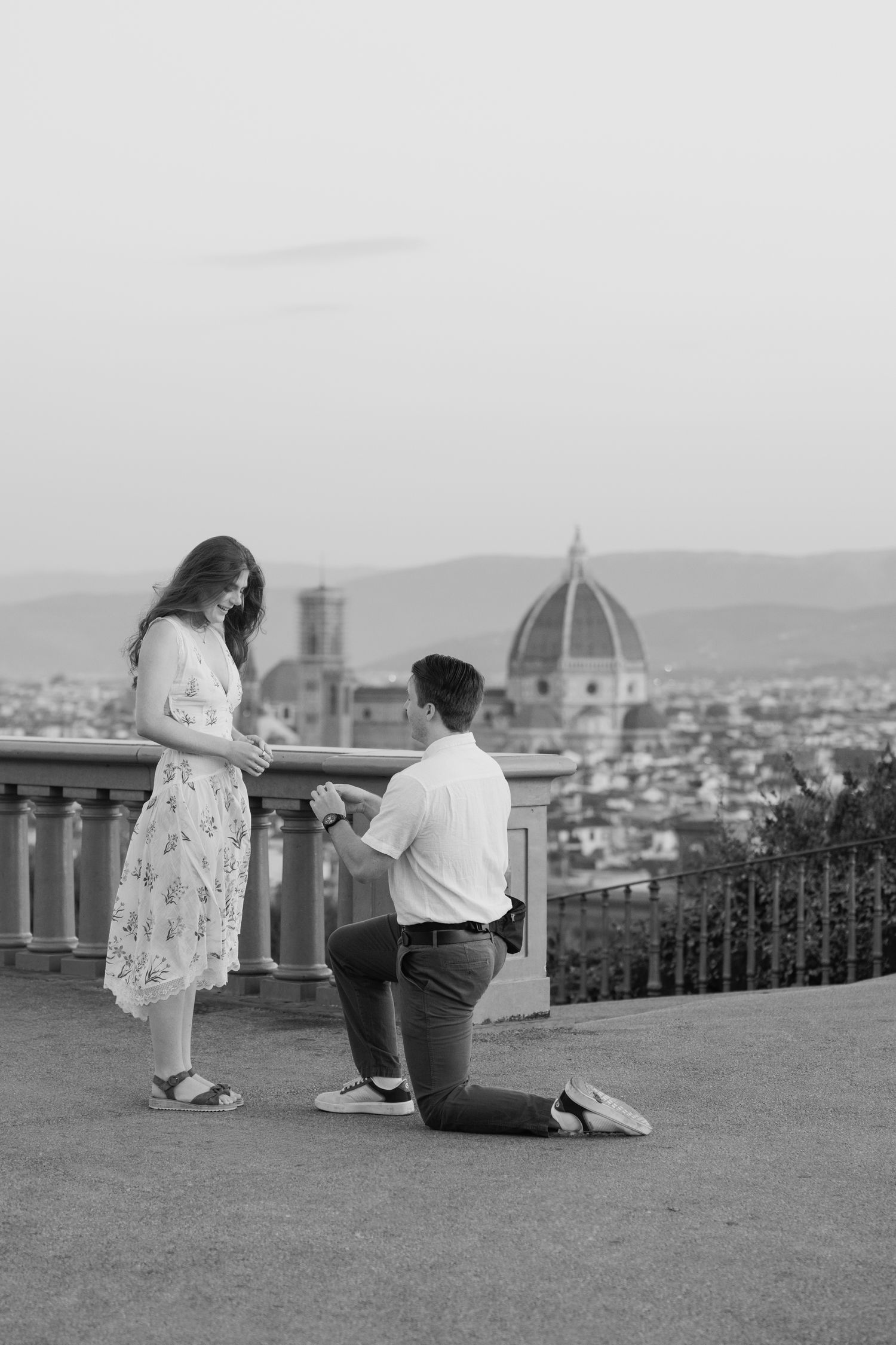 Man proposes on one knee to woman with Florence cathedral dome skyline backdrop in black and white.