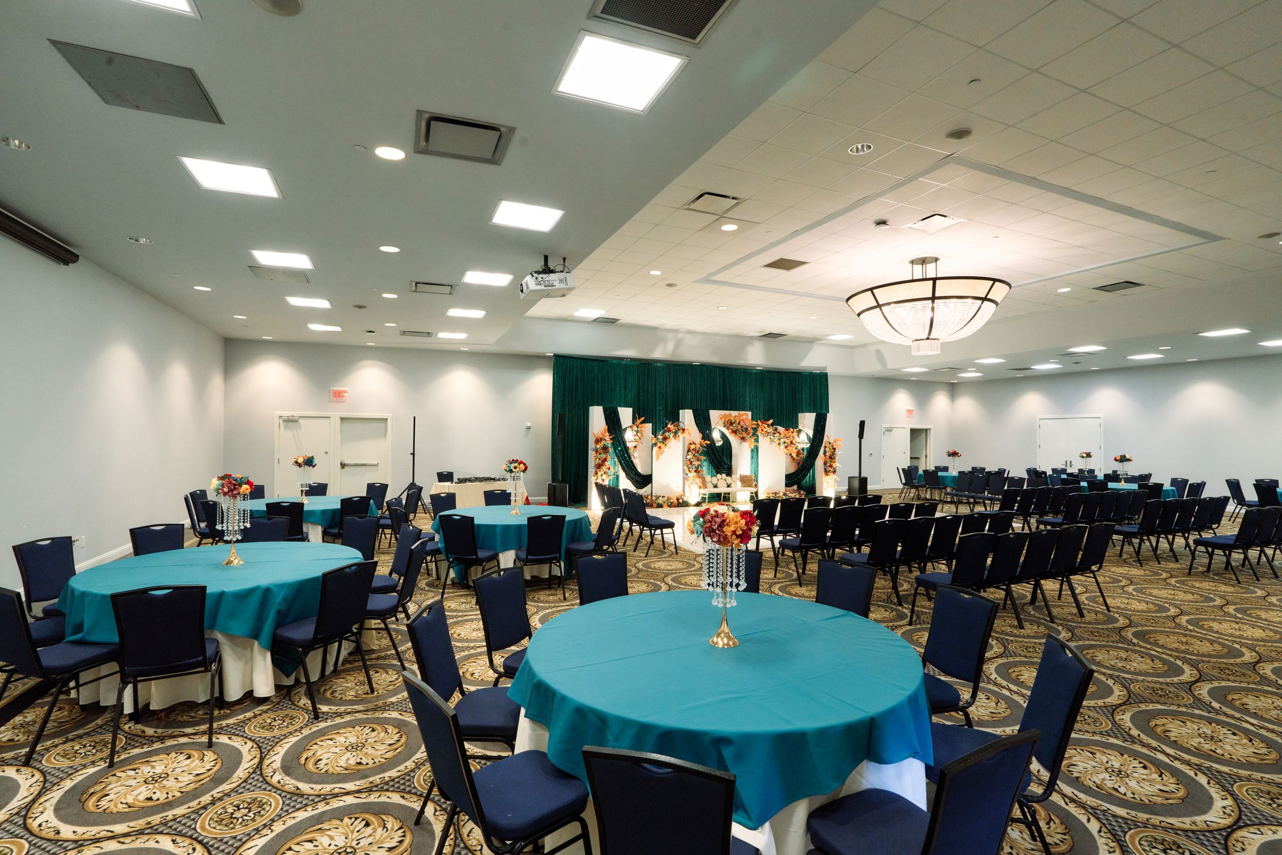 Elegant banquet hall with teal tablecloths, blue chairs, and floral arch backdrop for a wedding reception.