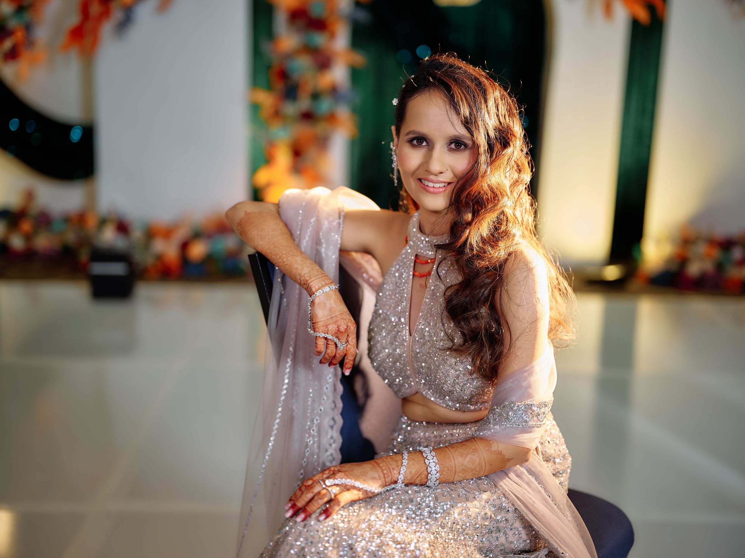 Woman in elegant silver embroidered lehenga smiling at a festive Indian celebration event.