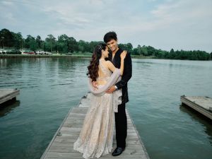 Couple in formal attire sharing a romantic moment on a wooden dock overlooking a serene lake.
