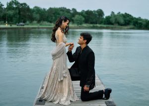 Man proposing to woman in elegant dress on a wooden dock by a serene lake in a romantic outdoor setting.