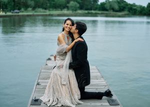 Couple in elegant attire sharing a romantic kiss on a wooden dock by a serene lake.