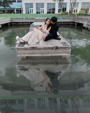 Couple in formal attire sitting on a dock over reflective water at an outdoor wedding venue.