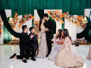 Wedding couple sharing kiss on dance floor surrounded by guests in colorful floral decorated venue.