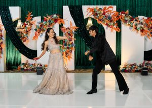 Couple dancing at an Indian wedding reception with colorful floral backdrop and green sequin curtains.