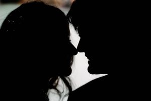 Romantic silhouette of couple facing each other in intimate moment against dark background.