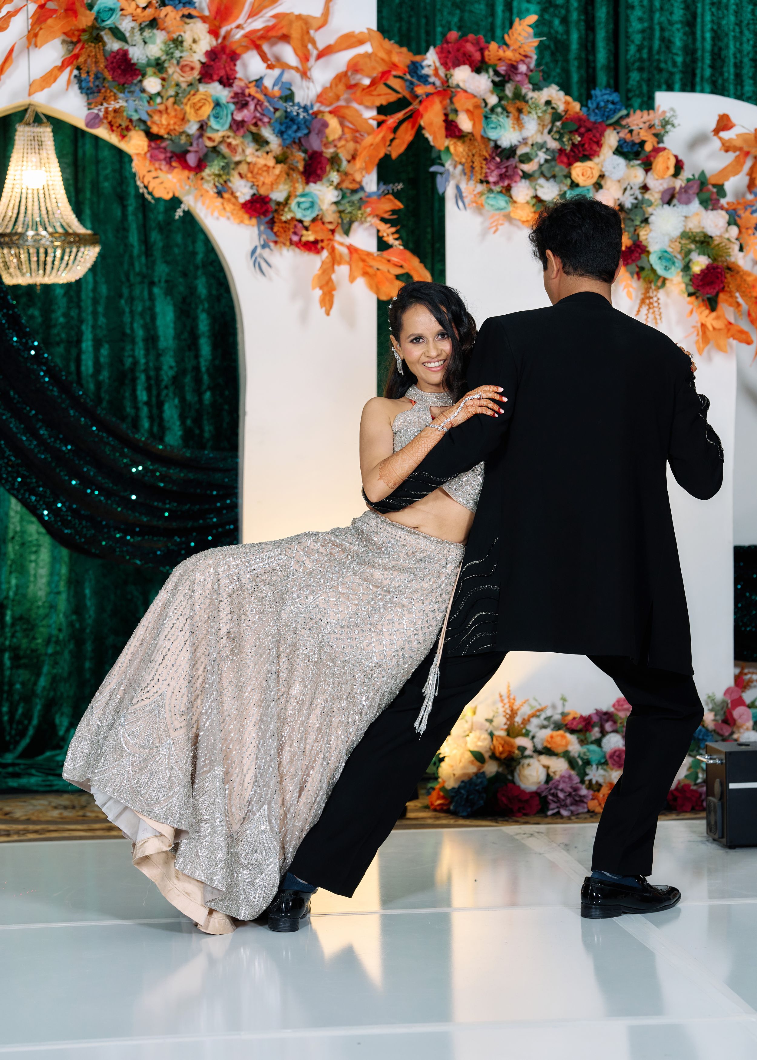 Couple performs dramatic dance dip on white floor surrounded by vibrant orange and red floral arrangements.