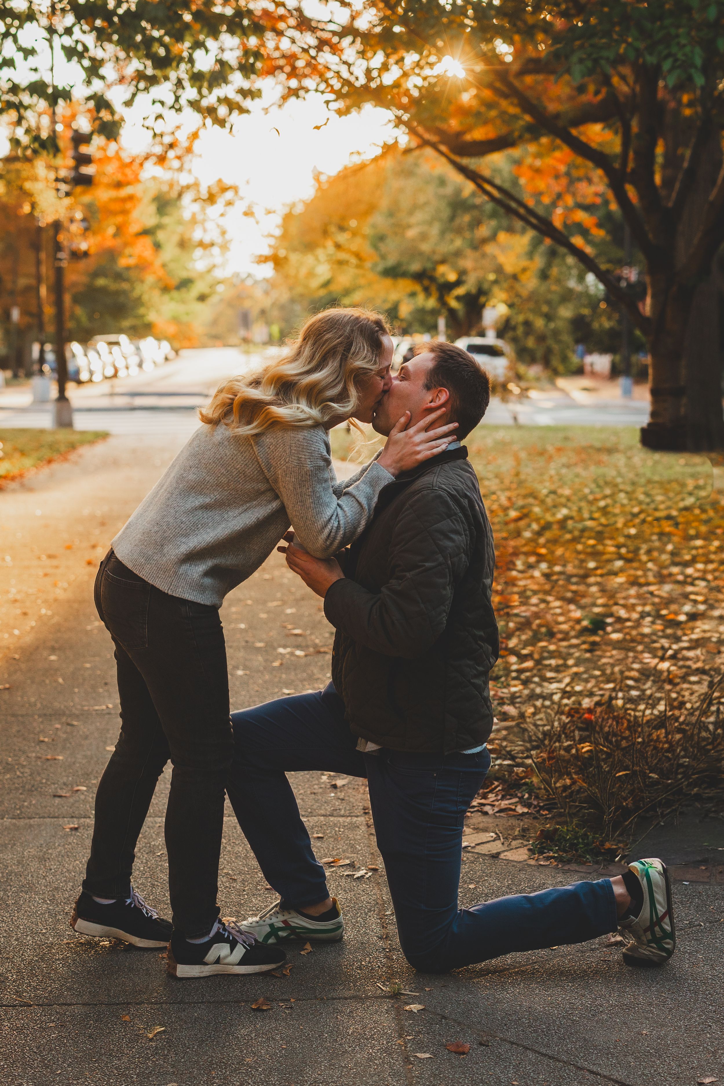 Couple sharing a romantic kiss during a marriage proposal in a scenic autumn park with colorful fall foliage.