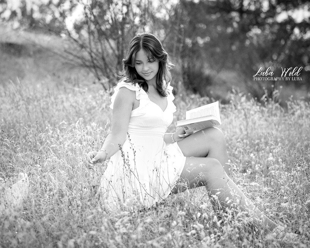Black and white portrait of a senior girl in white dress sitting in the grass field by photographer Luba Wold in Post Falls