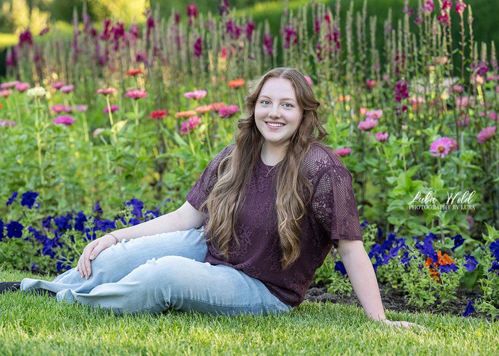 Spokane senior girl sitting by a flower bed in Manito Park by photographer Luba Wold in Post Falls