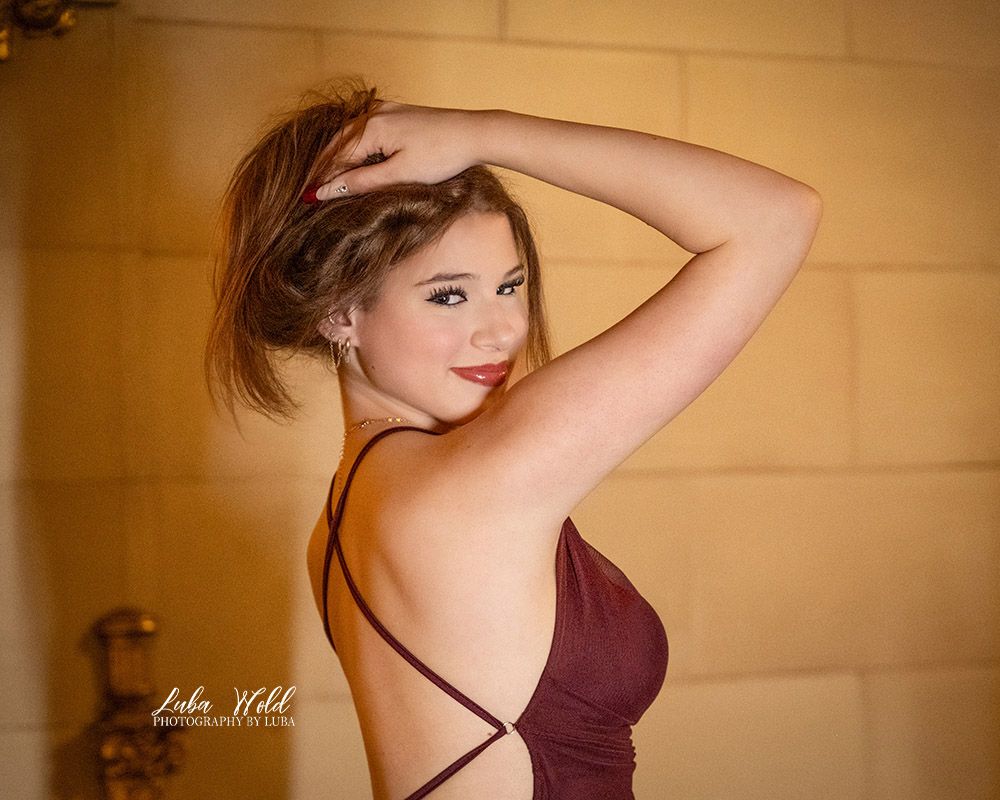 Senior girl in a beautiful fancy dress looking at photographer Luba Wold holding her hair in Spokane Davenport Hotel