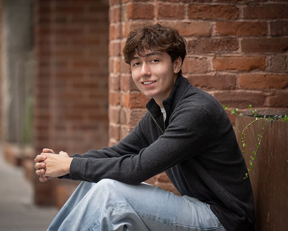 Senior boy young man in downtown Spokane sitting by a brick building by photographer Luba Wold
