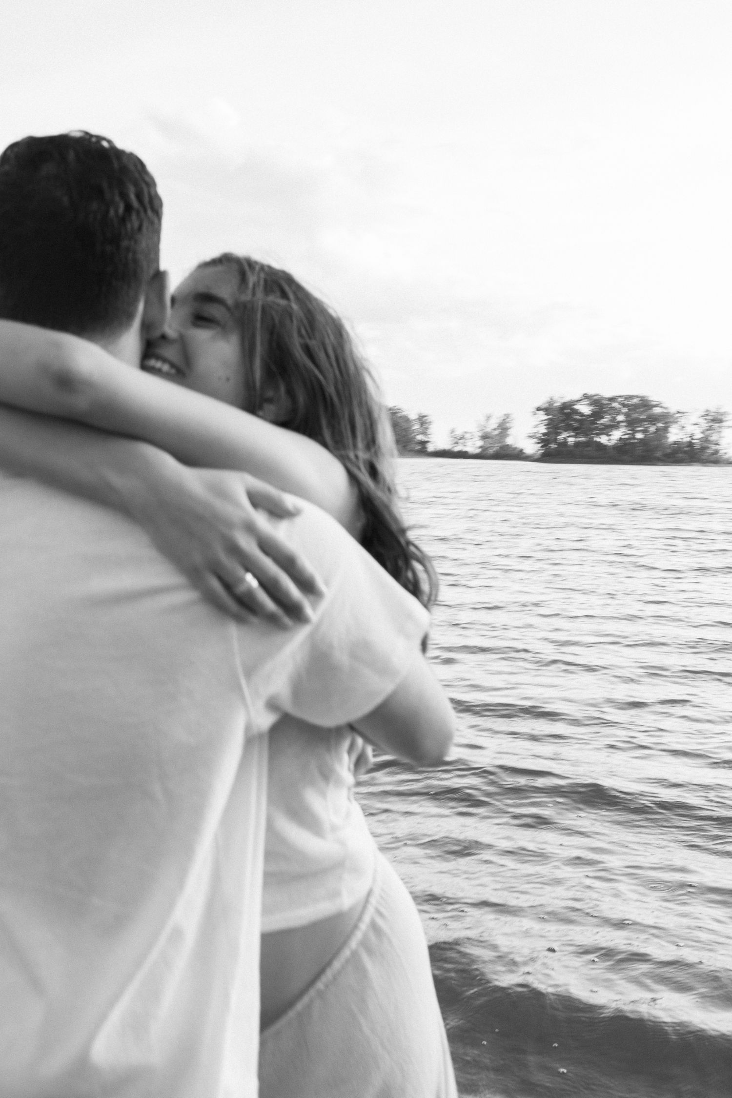 Black and white maternity session of an expecting couple embracing by the water at sunset in Montreal.