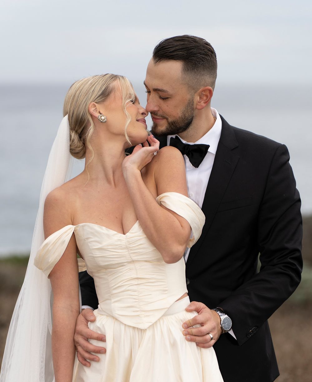 A romantic wedding moment captured outdoors with the bride in an off-shoulder cream gown and groom in classic black tuxedo.