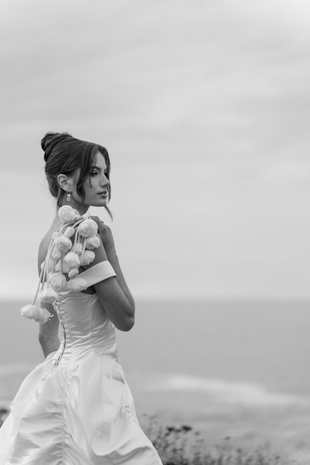 A bride in a flowing white dress runs joyfully along a scenic hilltop overlooking the ocean on her wedding day.