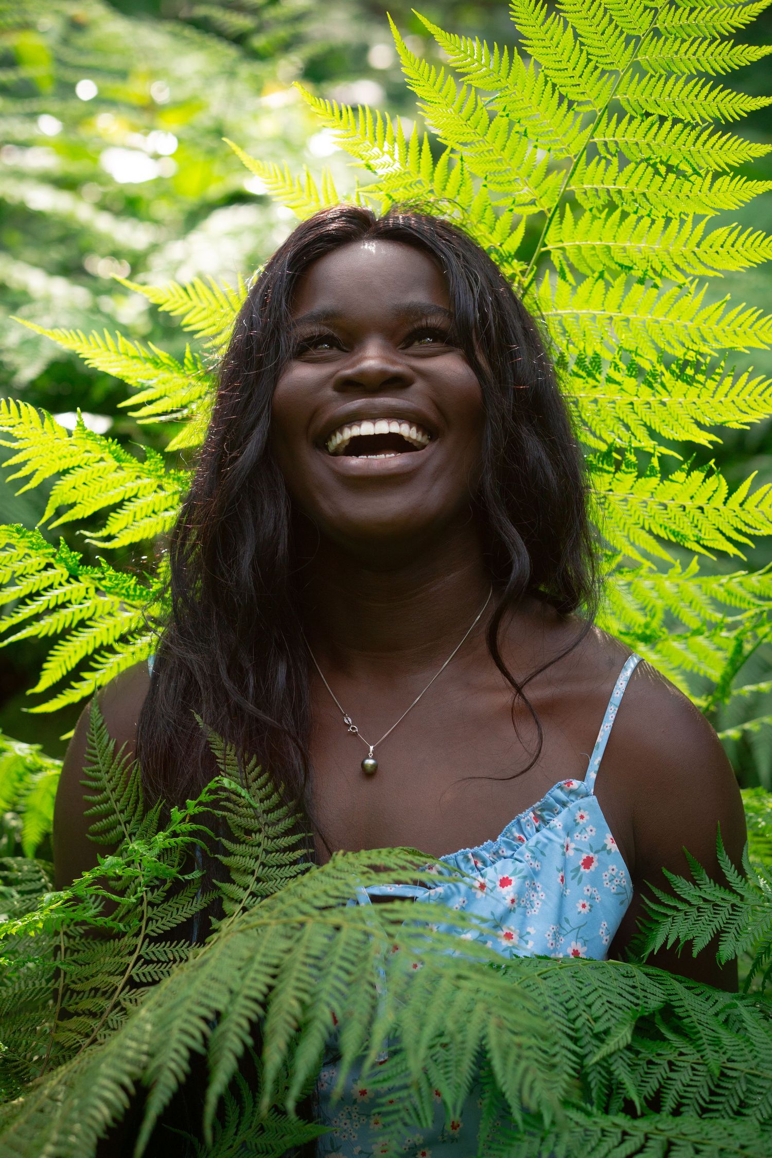 A joyful expression surrounded by vibrant green fern leaves in a sunlit forest setting.