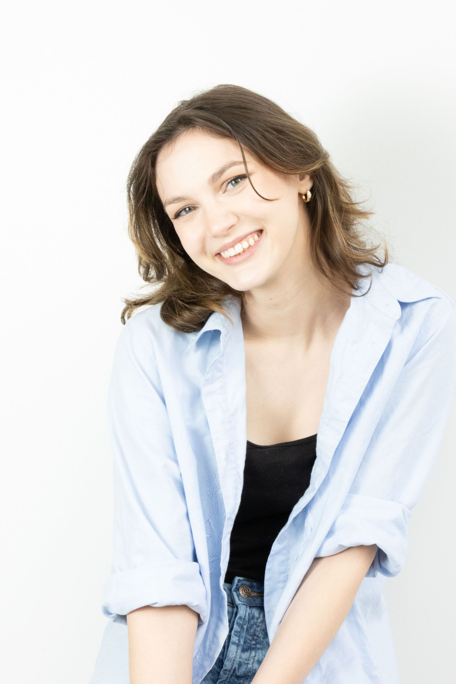 A smiling young woman with wavy brown hair wears a blue shirt over a black top.