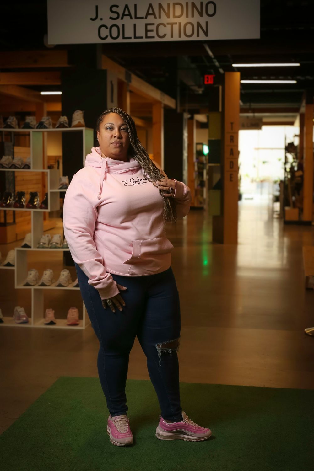 Athletic woman in pink hoodie and jeans poses in sportswear collection display area.