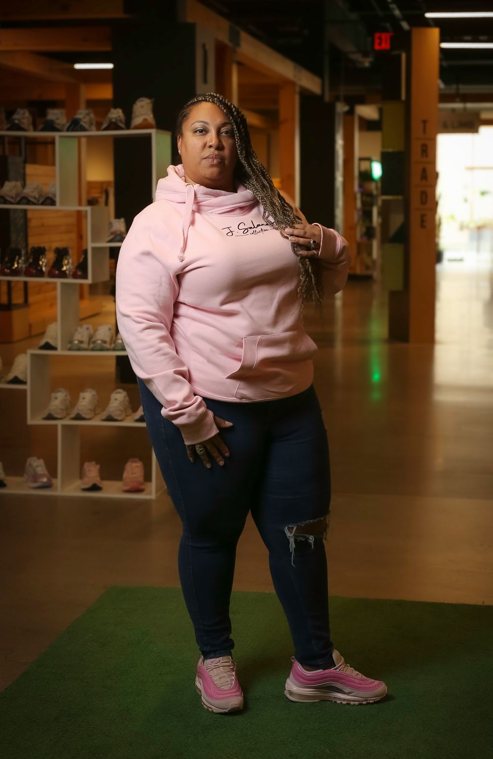 Person wearing a pink hoodie and ripped jeans poses in a casual stance at what appears to be a shoe store.