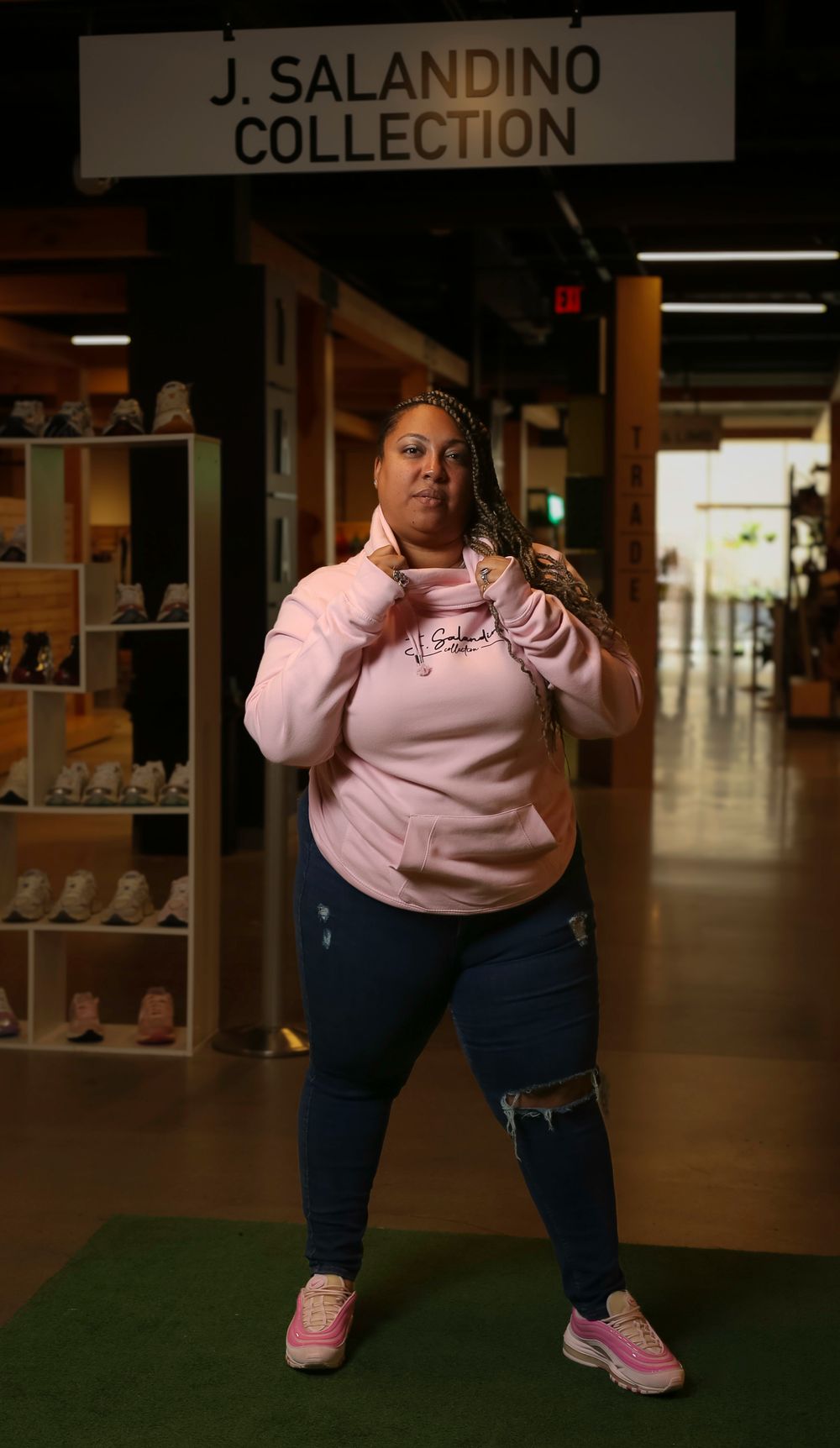 A person poses in front of the J. Salandino Collection sign wearing a pink sweatshirt and distressed jeans.