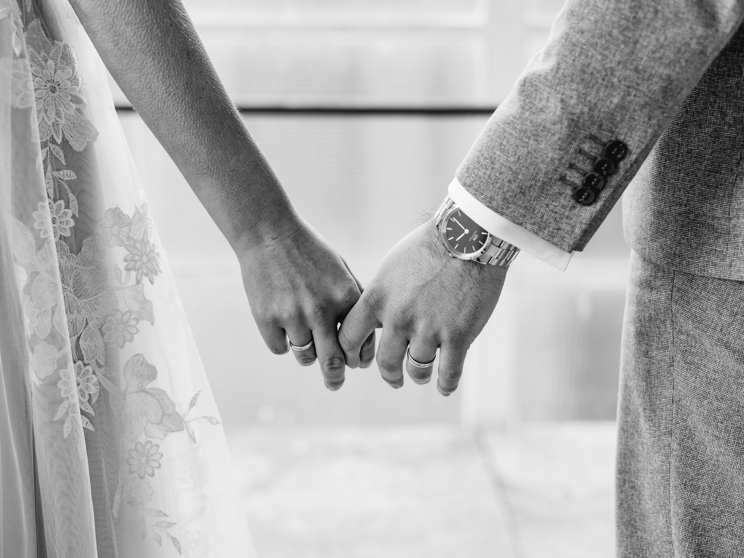 Black and white close-up of hands showing intricate lace details on wedding attire.