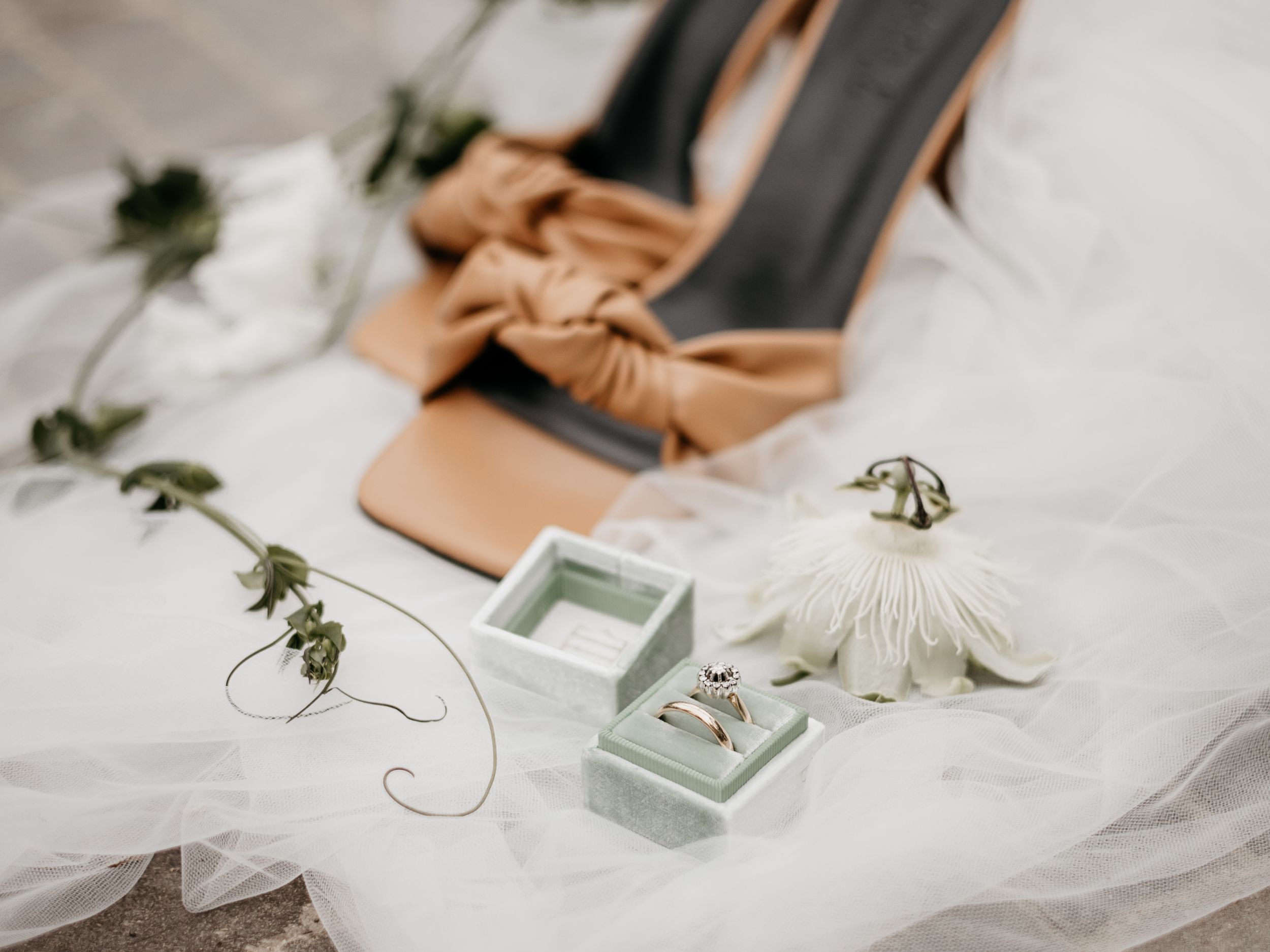 Wedding rings and delicate details displayed on white fabric with botanical elements.