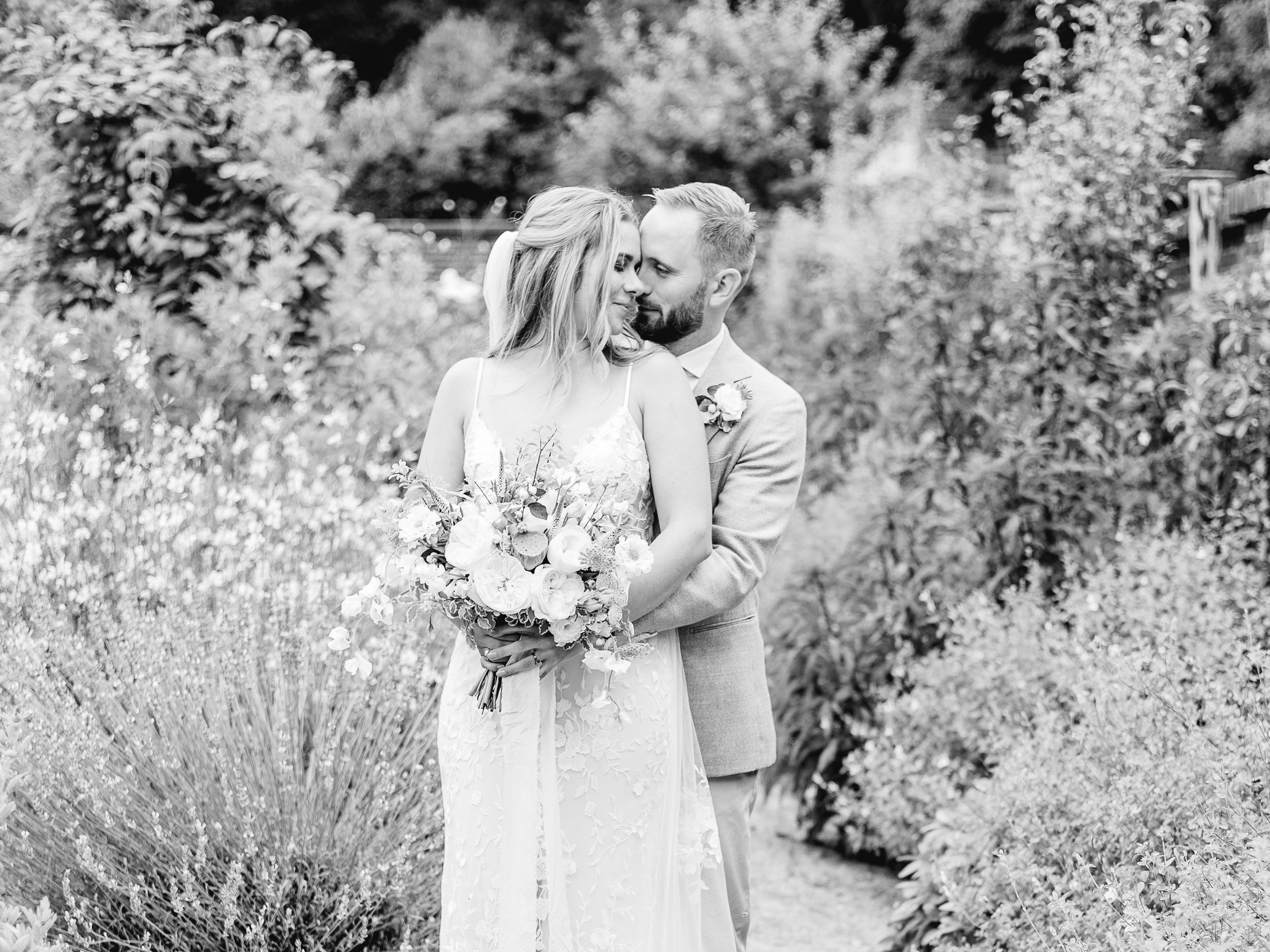 Wedding couple poses in a serene garden setting surrounded by white flowers.