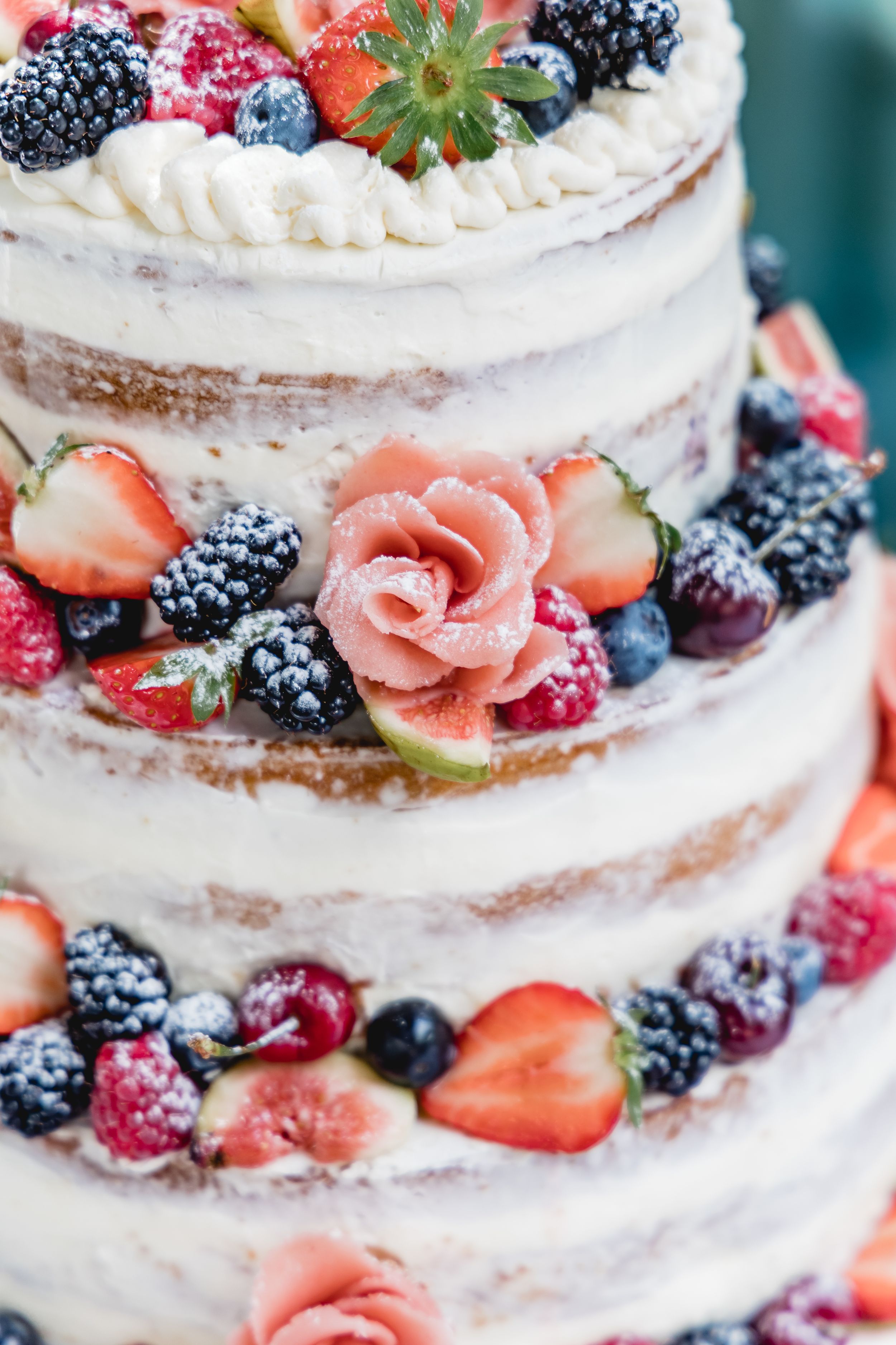 Rustic naked wedding cake decorated with fresh berries and floral accents.