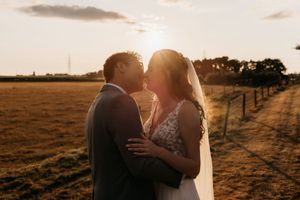 Sunset wedding portrait silhouette against golden sky and countryside landscape.
