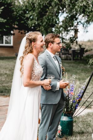 Joyful outdoor wedding portraits with the couple laughing among summer flowers.