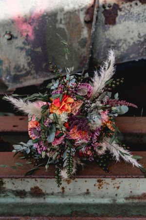 Vibrant floral arrangement with feathers and colorful blooms on rustic metal surface.
