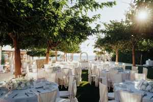 Elegant outdoor wedding reception setup with white tables and chairs under trees at sunset.