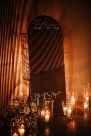 Romantic wedding reception setup with candlelit tables and elegant black signage in warm ambient lighting.