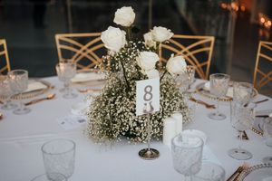 Elegant wedding reception table with white roses and baby's breath centerpiece, gold chairs, and table number eight.