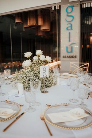 Elegant wedding reception table setting with white roses, baby's breath, gold charger plates and crystal glassware.