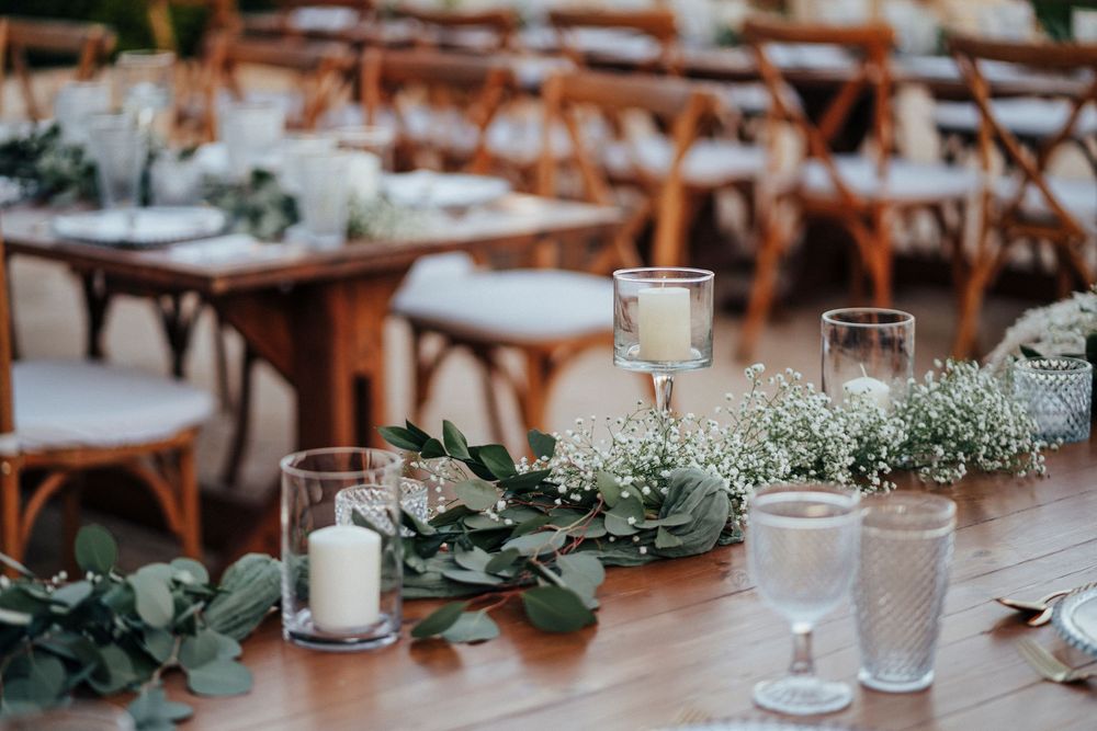 Wedding reception tables decorated with white floral centerpieces and greenery garlands in an elegant outdoor setting.