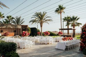 Outdoor wedding venue setup with white chairs and palm trees against a clear sky at sunset.