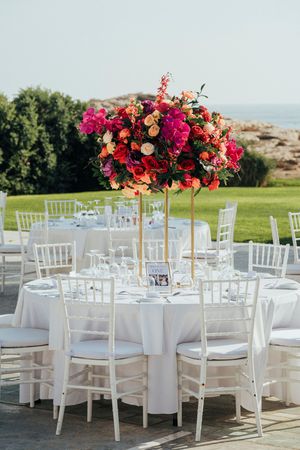 White chiavari chairs and round tables decorated with vibrant pink and orange floral centerpieces for an outdoor wedding reception.