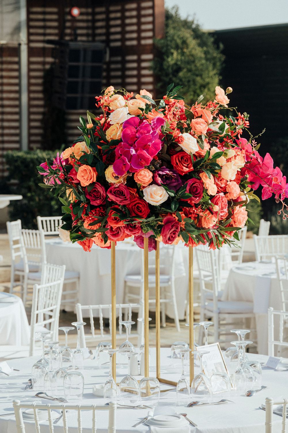 Elegant outdoor wedding reception tables decorated with tall pink and coral floral centerpieces and white chiavari chairs.