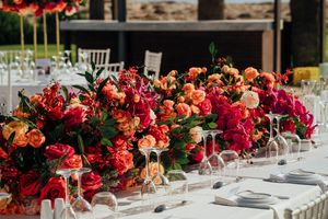 Elegant wedding reception table decorated with vibrant red and orange floral arrangements and crystal glassware.