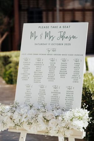 Elegant wedding seating chart displays with white floral decorations and guest names printed on clear acrylic stands.