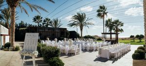 Panoramic view of a beachfront path with palm trees, power lines, and white chairs set up for an outdoor event.