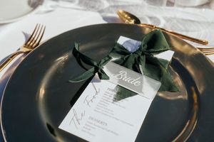 Elegant wedding place settings with gold cutlery, white plates, and greenery decorations on a dark tablecloth.