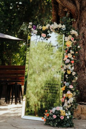 A decorative mirror with floral arrangements and text displays create an elegant outdoor photo opportunity setup.
