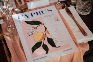 Wedding reception table settings with pink floral menus and elegant glassware on white tablecloth.