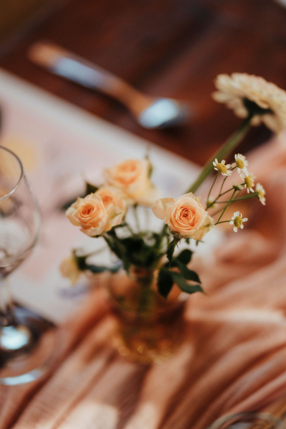 Peach roses and delicate white flowers arranged in wedding centerpieces on a wooden table with warm lighting.