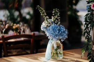Rustic wedding reception tables decorated with light blue hydrangeas in mason jars and greenery garlands.
