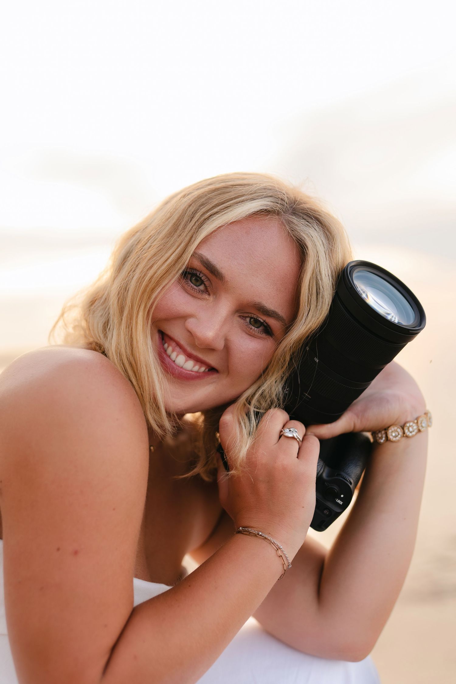 A photographer in black attire holding a camera in a warmly lit wooden interior space.