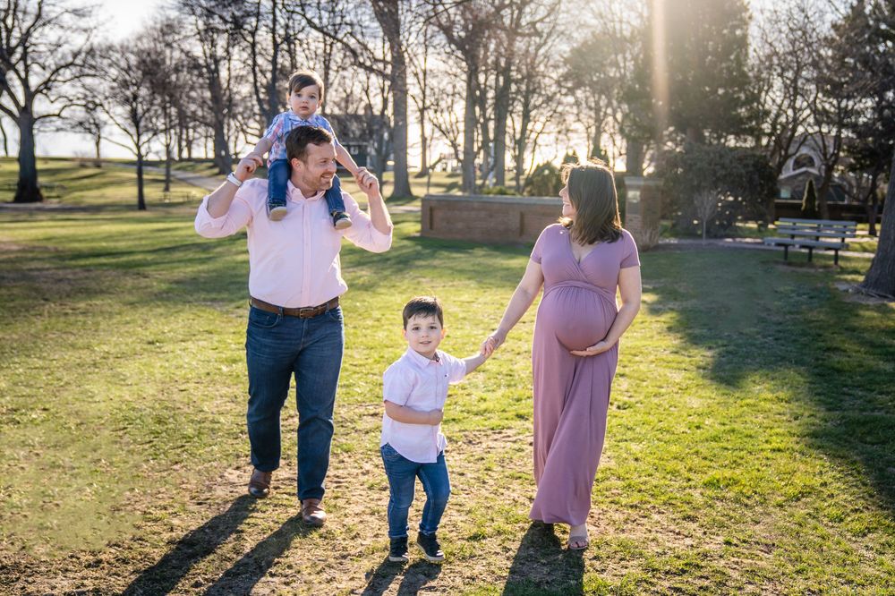 A family walks together on grass in a park during golden hour sunlight.